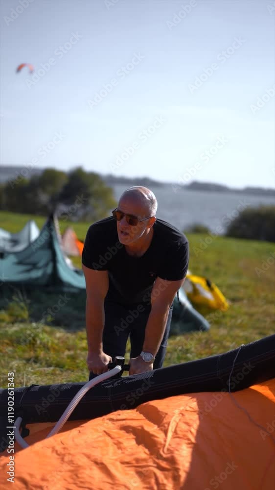 A man in wetsuit pumps up a kiteboarding kite on a beach