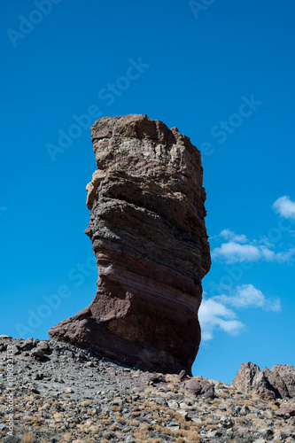 A large rock formation sits on a rocky hillside. The sky is clear and blue, and the sun is shining brightly. The rock formation is tall and has a unique shape photo