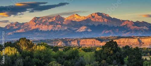 Majestic sunset illuminating a mountain range with foreground trees and valley.