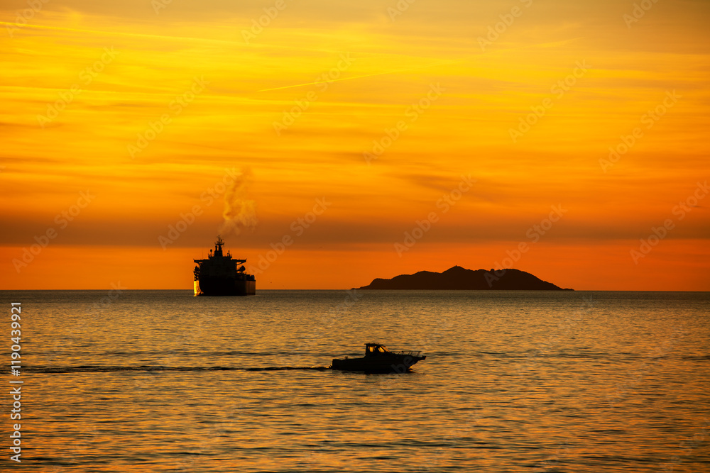 Fototapeta premium Sunset over the ocean with a cargo ship and a small motor boat in the backligh