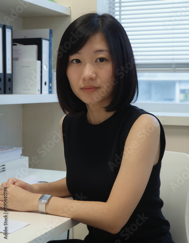 A photograph of an Asian woman with short black hair in a black sleeveless top, sitting at a desk. Free Download A photograph of an Asian woman with short black hair in a black sleeveless top, sitting at a desk. - GFXLoad