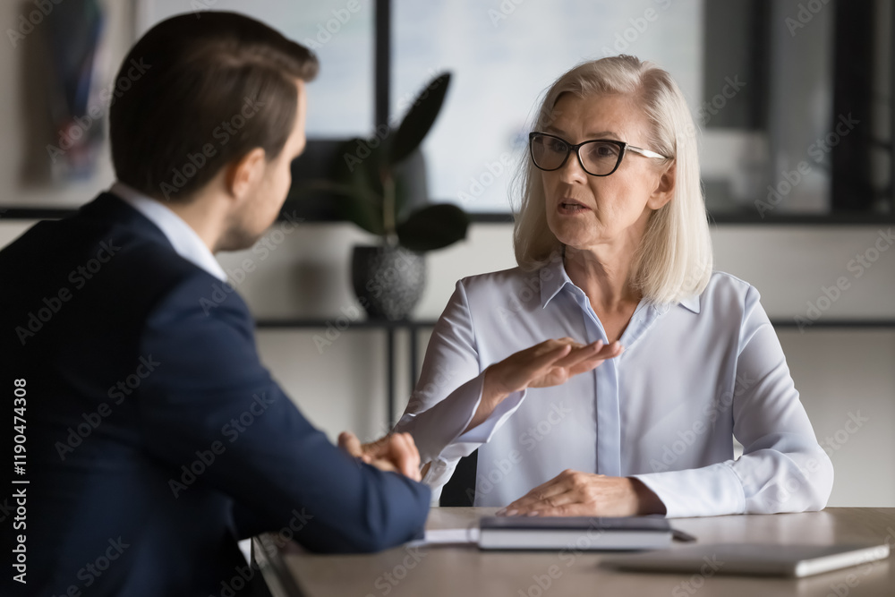 Obraz premium Confident mature business professional woman talking to younger male colleague, explaining work tasks, makes commercial offer to company client, share information, convince customer to buy services