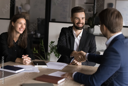 Two businessmen shaking hands across table, gesture of trust, agreement, closing of deal. Business parts gather in conference room, start or finalize negotiation feel satisfied, express mutual respect