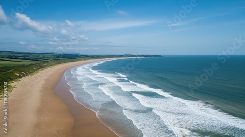 Aerial view of a scenic sandy beach with gentle waves curving along the coastline under a vibrant blue sky.