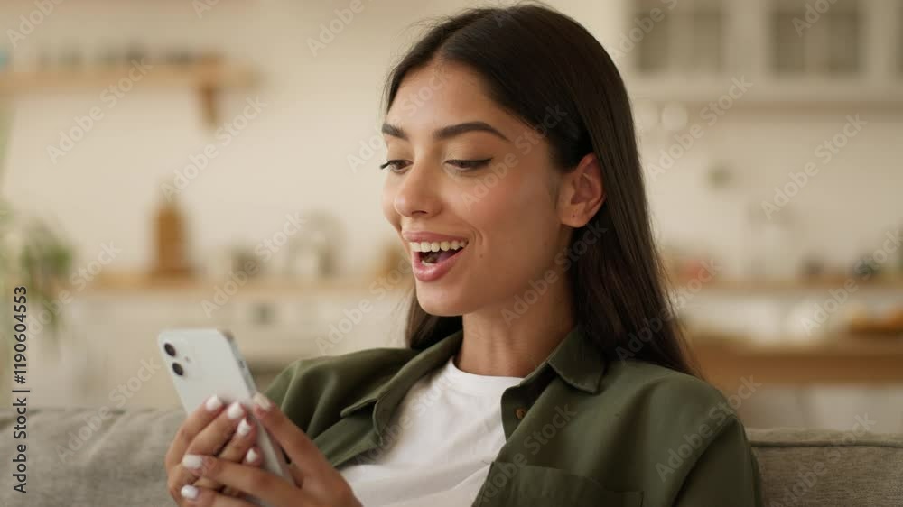 Happy smiling positive amazed wonder surprised Indian woman Arabian female ethnic girl browsing social media smartphone online using mobile phone chat scrolling at home good news offer achieve say wow