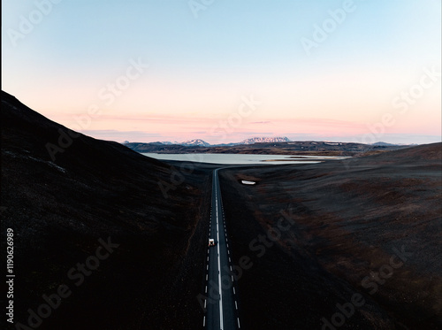 View from above, stunning aerial view of a car on a beautiful road passing through a dramatic landscape with a lake and snowy mountains in the distance, Iceland