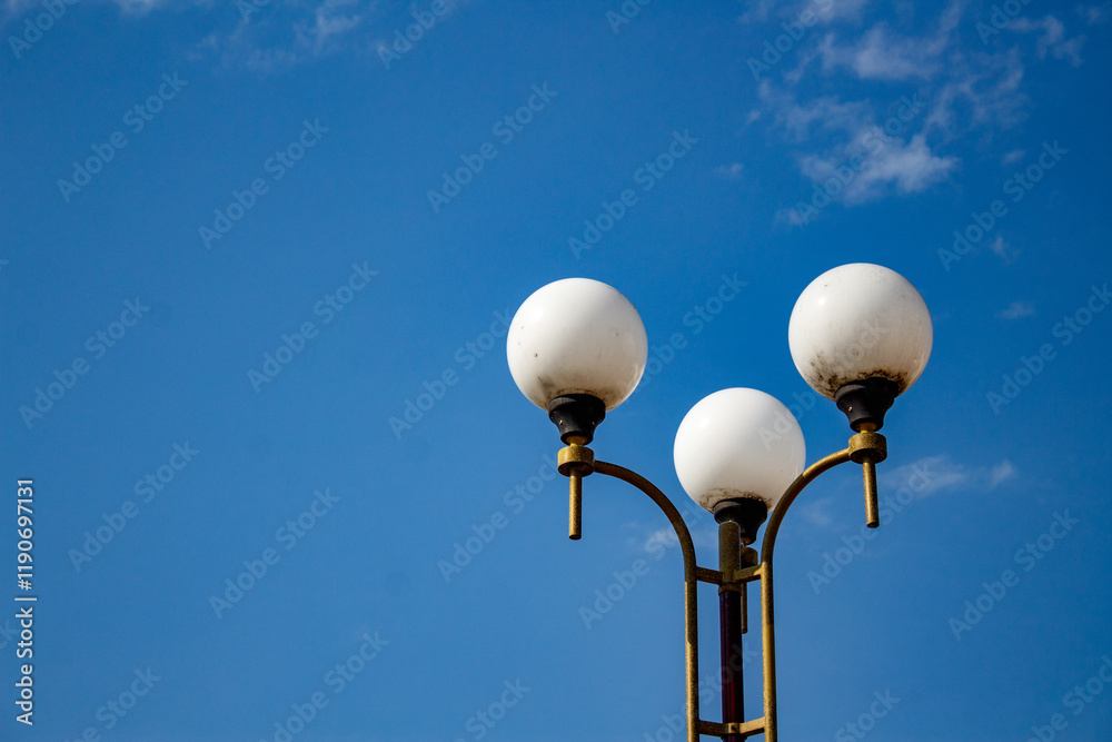 Three white lamps on a street light against a blue sky Three white lamps on a street light against a blue sky