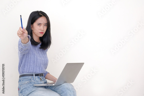 A young woman is offering a pencil with a serious expression; a laptop on her lap photo