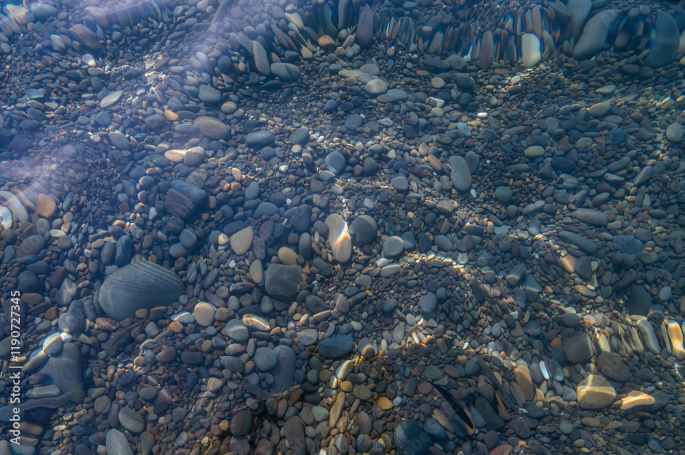 Underwater pebble backgrounds. Colorful stones sea bottom in the sun rays. View from above through clear water. Seascape wallpaper texture. Defocus.