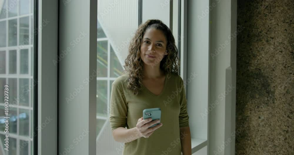 Portrait of Pretty Latin Female in Window holding Phone and Looking to camera Portrait of Pretty Latin Female in Window holding Phone and Looking to camera