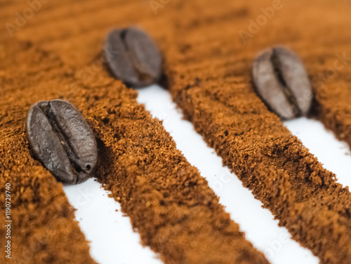 3 coffee beans make a white stripe on top of a sprinkle of coffee grounds on a white background photo
