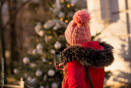 girl in pink hat stainng with her back winter christmass tree female lady woman red coat making photos on smartphone 