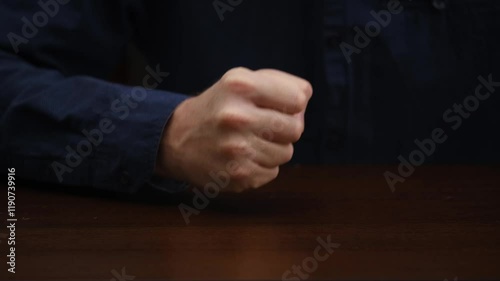 close-up male hand lying on table, slowly clenching into fist and knocking hard on table. hand gesture disappointed, angry businessman.