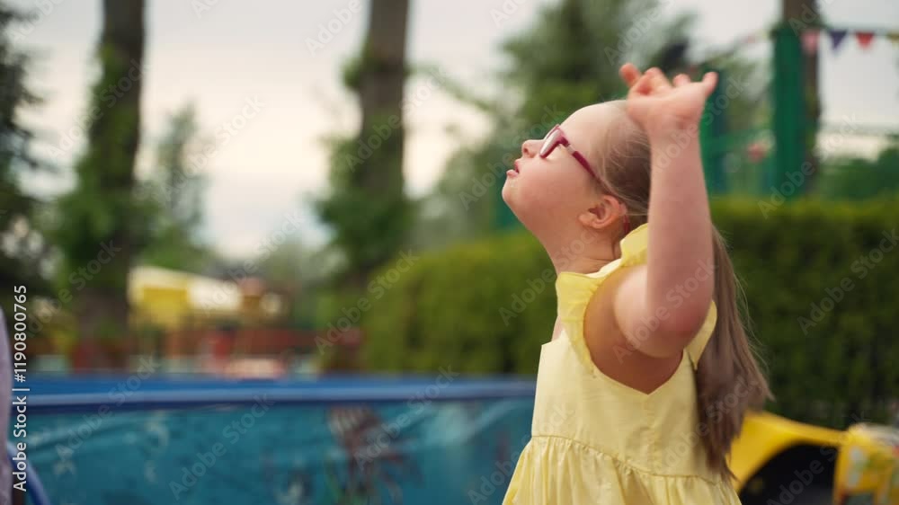 Girl with Down syndrome enthusiastically performs dance she learned in kindergarten. She moves gracefully in amusement park, surrounded by greenery. Concept joy, inclusion and childhood creativity