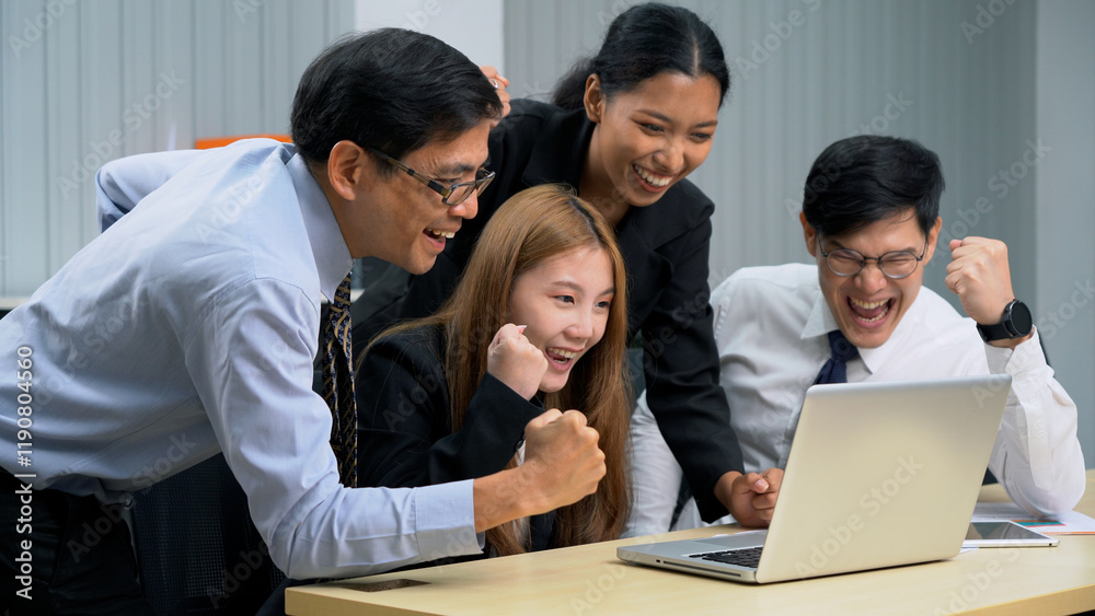 Group of happy asian business people sitting on a table raised fists cheering at laptop celebrating achievement goals to success in meeting at office Group of happy asian business people sitting on a table raised fists cheering at laptop celebrating achievement goals to success in meeting at office
