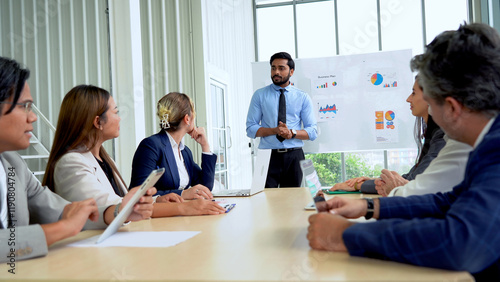 Young indian business manager standing and presenting to multiracial group of diversity colleagues in front of white board in meeting at boardroom in office . leader