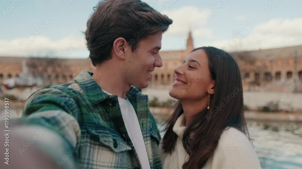 Happy young couple man and woman kissing, taking selfie while standing on bridge Happy young couple man and woman kissing, taking selfie while standing on bridge