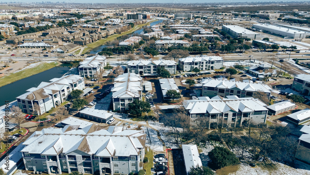 Fototapeta premium Modern riverside apartment complex buildings in snow cover near Lewisville warehouse fulfillment center, residential neighborhood houses and downtown Dallas Texas in distance background, aerial
