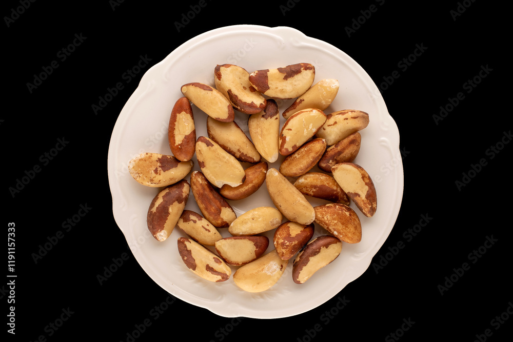 Brazil nuts without shells on a white ceramic plate on a black background, close-up, top view. Brazil nuts without shells on a white ceramic plate on a black background, close-up, top view.