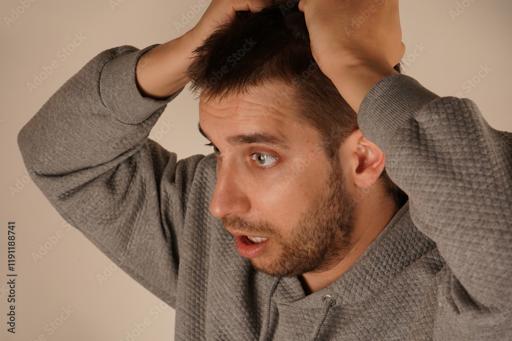 Fototapeta premium His face reflects a moment of suffering. The pose creates an irresistible feeling of mental tension. Holding his hair in his fist, the man shows clear signs of tension or stress.