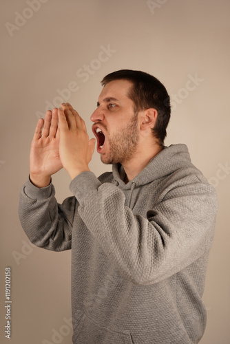 A young man with dark hair places his hands near his mouth, resembling a megaphone. His enthusiastic pose suggests he is delivering an energetic shout. The scene captures his dramatic gesture. photo