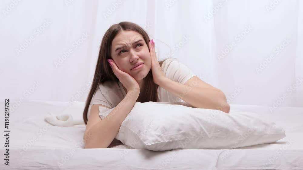 A young beautiful girl hears loud sounds from her neighbors and covers her head with a pillow to avoid the noise. A young beautiful girl hears loud sounds from her neighbors and covers her head with a pillow to avoid the noise.