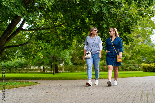 Two smiling mature women walking in city park. Meeting of friends. Walk in park	 photo