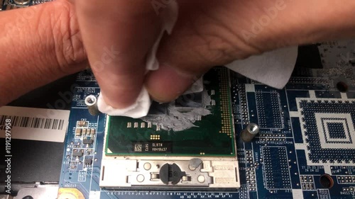 A computer technician hand carefully cleans the remaining thermal paste on a laptop processor using a tissue