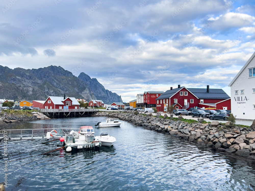 Naklejka premium A scenic view of Henningsvær in Lofoten Islands, northern Norway, showcasing traditional buildings along the harbor with mountains in the background.