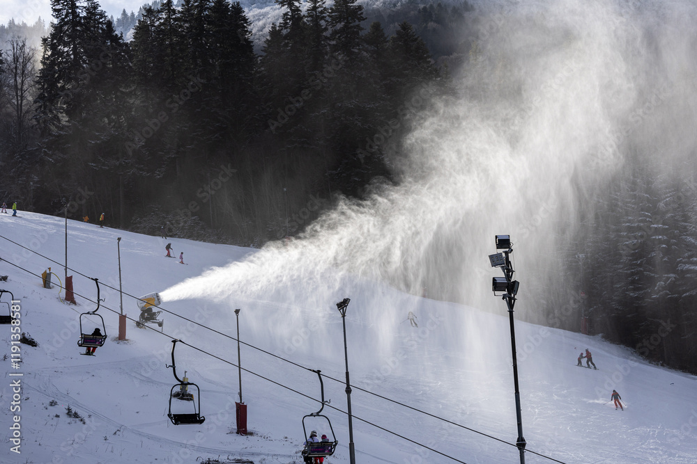 Winter ski resort. Beautiful view with clouds of snow created by the snow cannon machine. Tourist skiing on slopes. Winter sports.