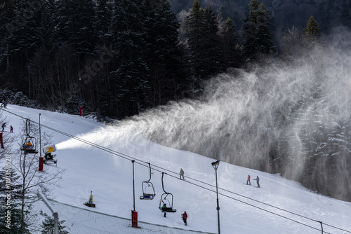 Obraz na płótnie Winter ski resort. Beautiful view with clouds of snow created by the snow cannon machine. Tourist skiing on slopes. Winter sports. w salonie