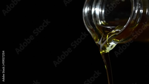 Extra virgin olive oil being poured out a clear glass bottle on a black background, close up, slow motion . Organic liquid flowing, copy space