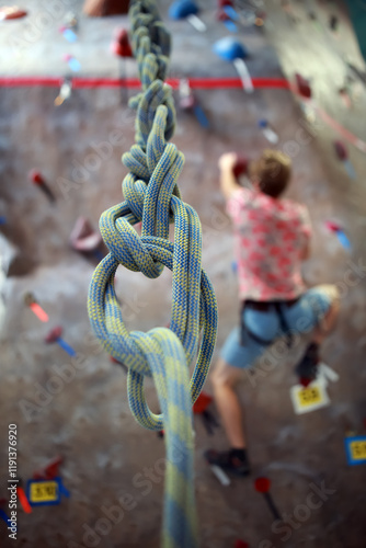 Young man climbing a rock wall at a gym, shallow focus on the looped belay rope