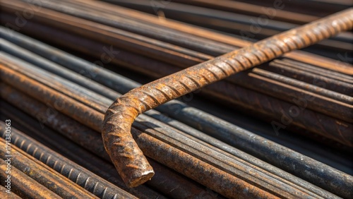 A closeup of a single rusted rebar bent at an angle its surface texture revealing years of exposure resting against a larger bundle of unblemished shiny rebar. photo