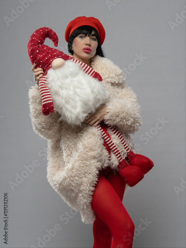 A young, beautiful woman in a white fashionable fur coat, red tights, and a red beret, holding a Finnish Santa toy. She has stunning black hair, adding elegance to the festive look.
 photo