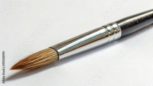 A medium closeup of a finetipped paintbrush capturing the delicate bristles splayed at the end showing variations in length and thickness while focusing on the metallic ferrule