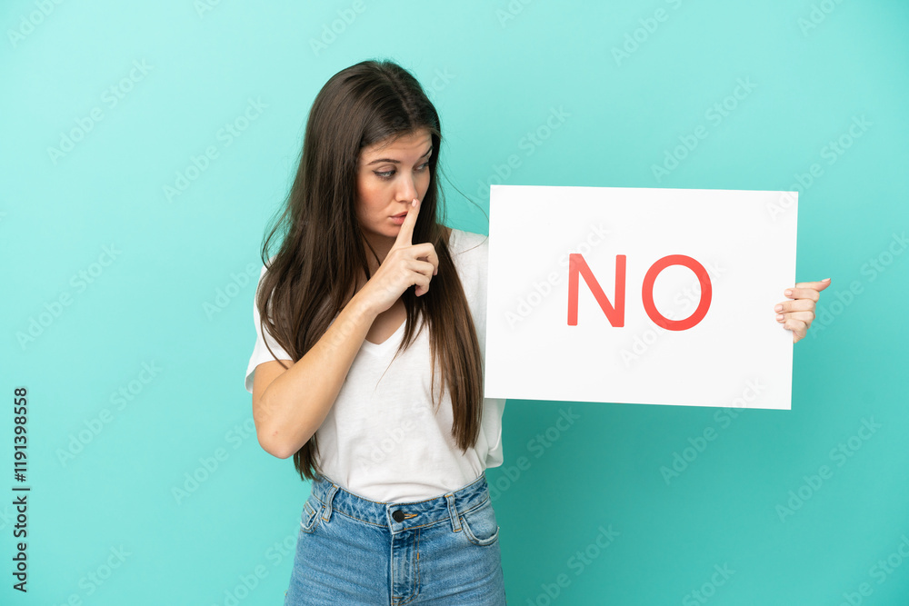 Young caucasian woman isolated on blue background holding a placard with text NO doing silence gesture Young caucasian woman isolated on blue background holding a placard with text NO doing silence gesture