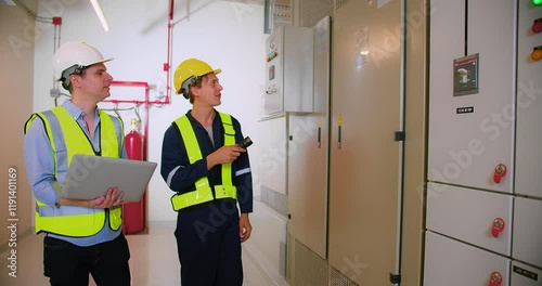 Engineers Collaborating in Industrial Control Room electrical control panel with Safety Gear and Equipment, Monitoring Systems, and Discussing Technical Operations for Efficient Facility Management