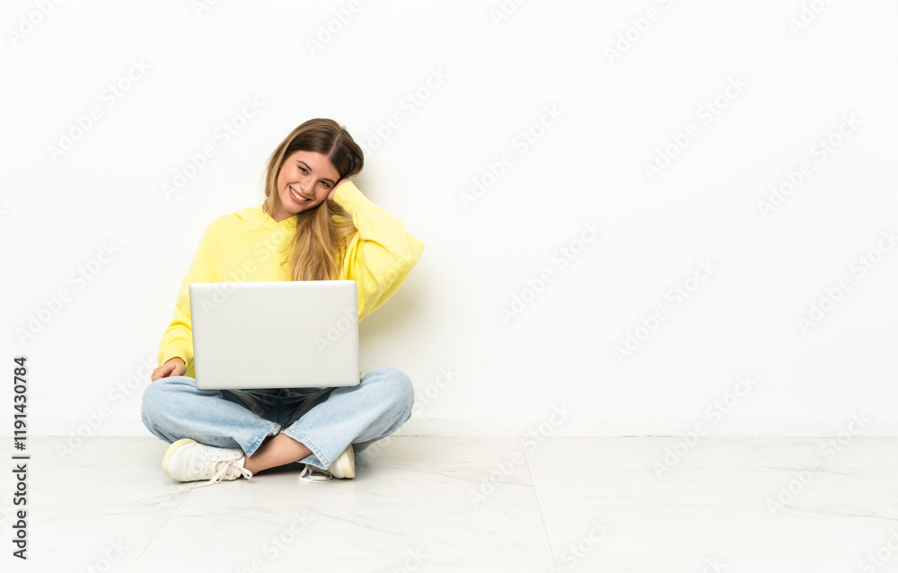 Young woman with a laptop sitting on the floor laughing
