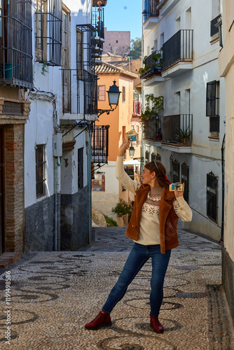 A girl holding tarot cards stands on a cobblestone street in Granada surrounded by traditional buildings under bright sunlight with a clear view ahead;