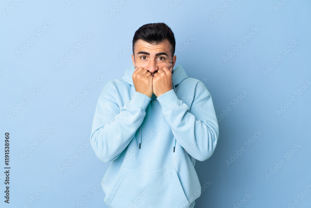 Caucasian man over isolated blue background nervous and scared putting hands to mouth Caucasian man over isolated blue background nervous and scared putting hands to mouth