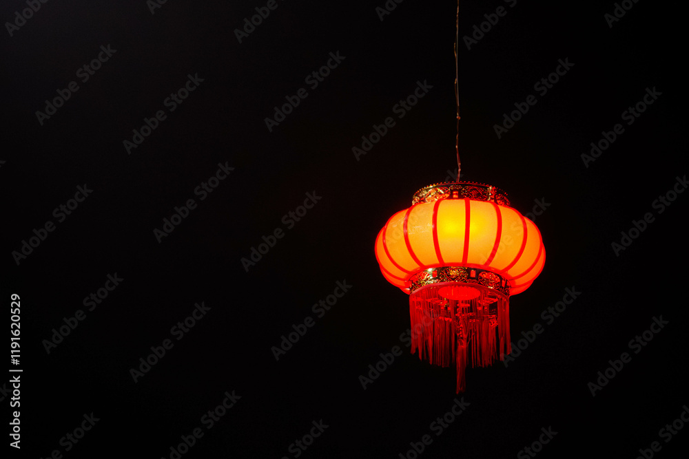 Obraz premium A glowing red Chinese lantern suspended against a dark black background, showcasing intricate patterns and warm illumination. Perfect for cultural, festive, or traditional design themes.