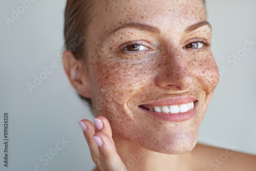 Fotografía Smiling woman with freckles and radiant hydrated skin, gently applying skincare soothing gel on her face, showcasing natural beauty in a close-up shot against a light background