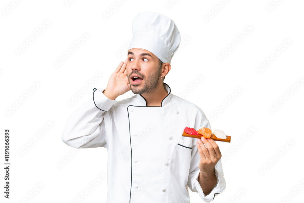 Young caucasian chef holding a sushi over isolated background listening to something by putting hand on the ear