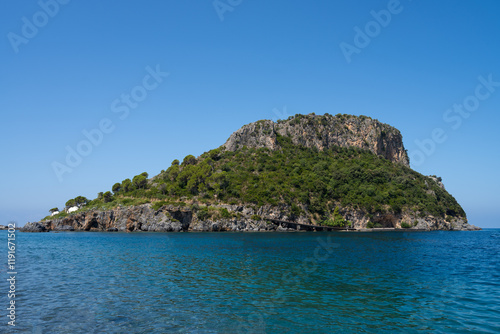 The island of Isola di Dino in Praia a Mare near Arco Magno in Calabria, Italy. There are many trees on the island. You can also see the clean blue sea in the foreground and a beautiful blue sky.