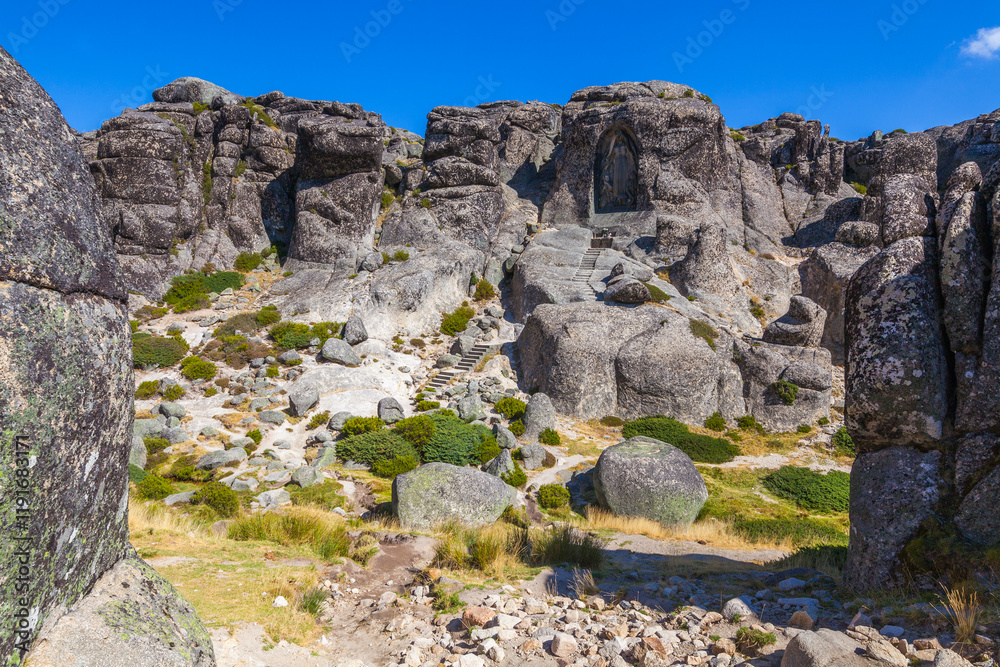 A carved image within a rock face, accessed by stone steps, creates a sense of sacred space and history against a clear blue sky A carved image within a rock face, accessed by stone steps, creates a sense of sacred space and history against a clear blue sky