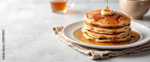 Delicious pancakes topped with butter and dripping maple syrup, evoking a warm and inviting breakfast scene, placed on a textured cloth beside a cup of syrup