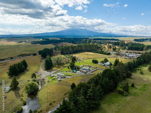 High-angle view of a rural farm, featuring buildings, pastures, and a mountain backdrop. Tranquil countryside scene. WAIOURU, MANAWATU-WANGANUI, NEW ZEALAND photo