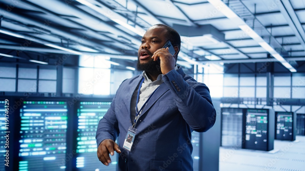 Fototapeta premium IT support worker in data center talking in phone call, doing yearly checkup. On field engineer chatting with manager in server hub during telephone call, monitoring servers infrastructure, camera B