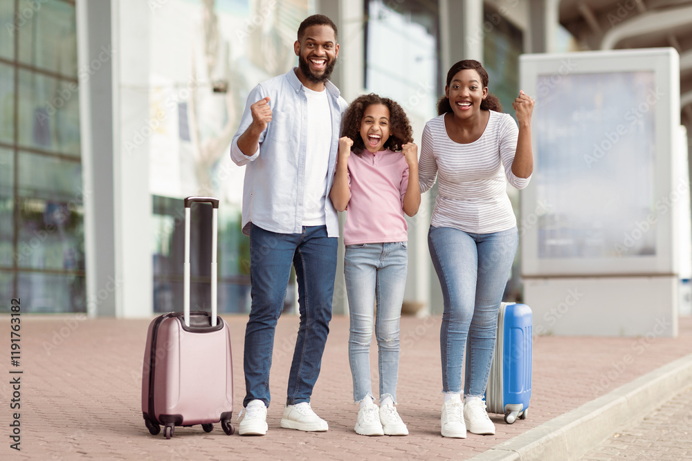 Fototapeta premium Holiday Trip After Lockdown. Full body length portrait of excited African American mum, daddy and daughter going on a journey. Family shaking clenched fists, making win gesture, standing near airport